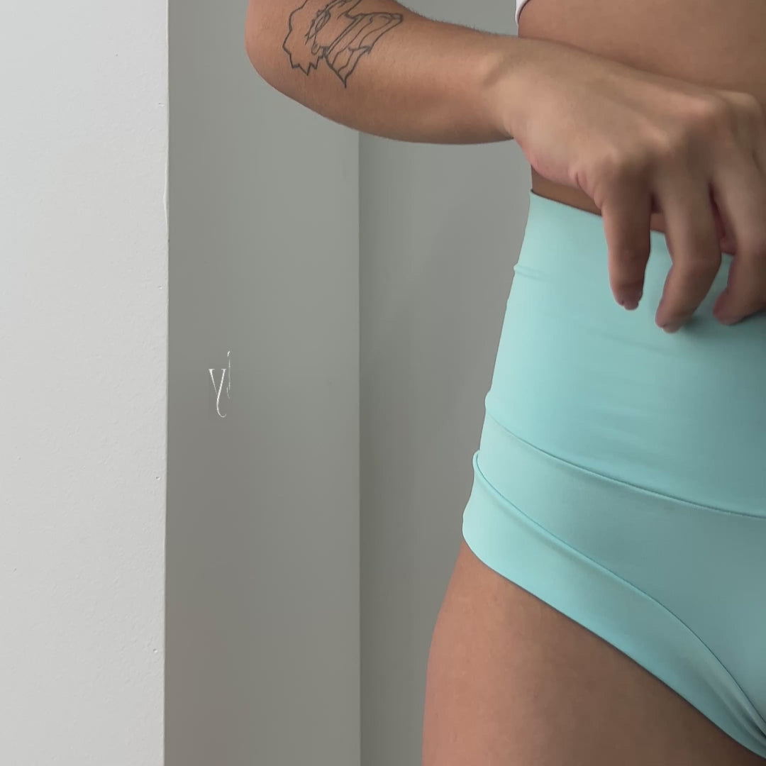 Mulher vestindo shorts curtos azul-claro de cintura alta mostrando vista lateral e detalhes do design.