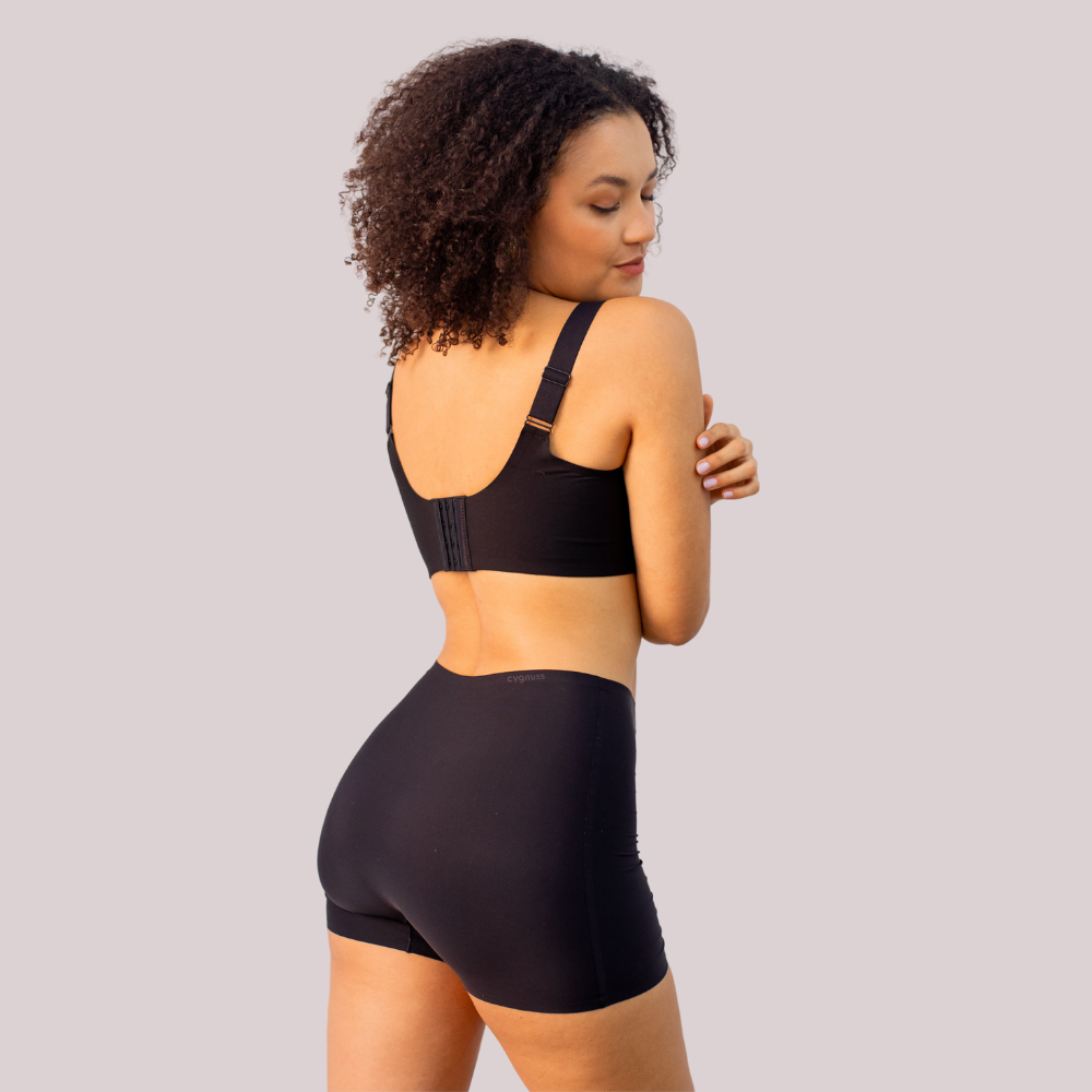  mulher usando o Short Segunda Pele Sem Costura na cor preta. A peça proporciona conforto e modelagem sem costuras, garantindo um ajuste perfeito e discreto para o dia a dia, com o logo da Cygnuss visível na parte superior.