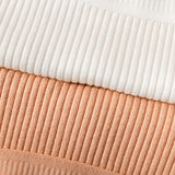 Close em tecidos canelados de calcinhas empilhadas, nas cores branca, terracota e bege claro. A imagem destaca a textura do tecido e o acabamento das costuras, transmitindo a maciez e qualidade do material.